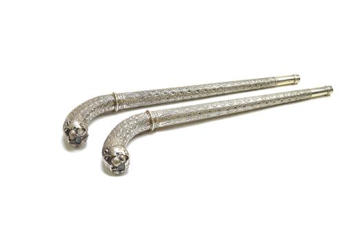 A pair of Indian white metal Choba staffs, late 19th century, each with tiger head terminals and a foliate cast tapering cylindrical handle, 60cm, (2)