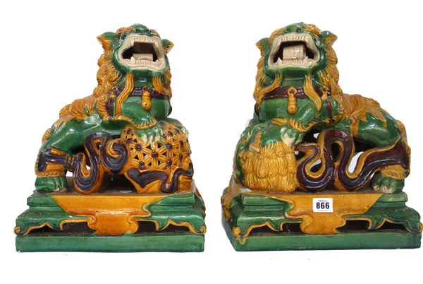 A pair of Chinese green and yellow glazed figures of Buddhistic lions, 20th century, modelled with a lion cub and brocade ball and raised on rectangul