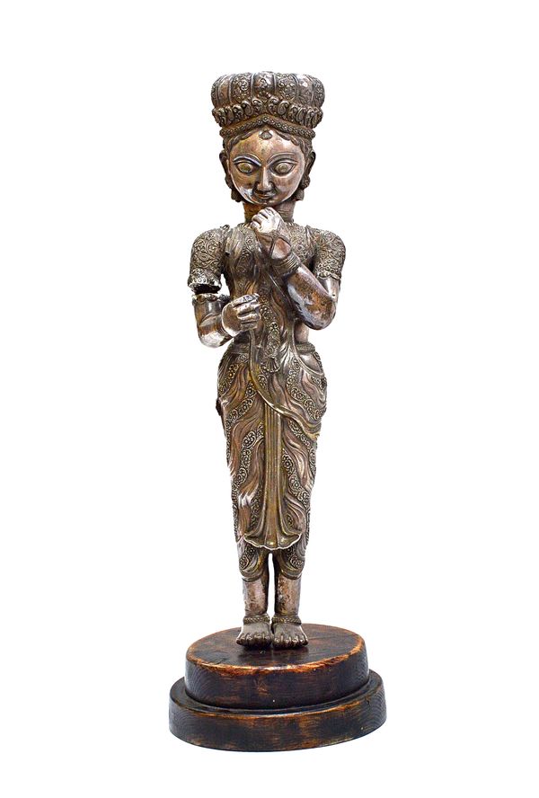 A repousse white metal Indian figure, 19th century, modelled and cast as a female attendant in florid foliate dress (a.f), 60cm high, on a later eboni