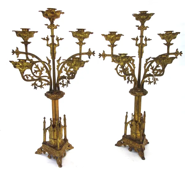 A pair of Gothic Revival brass five branch candelabra of foliate design, mounted over a triform shaped base and three feet, 56cm high, (2).
