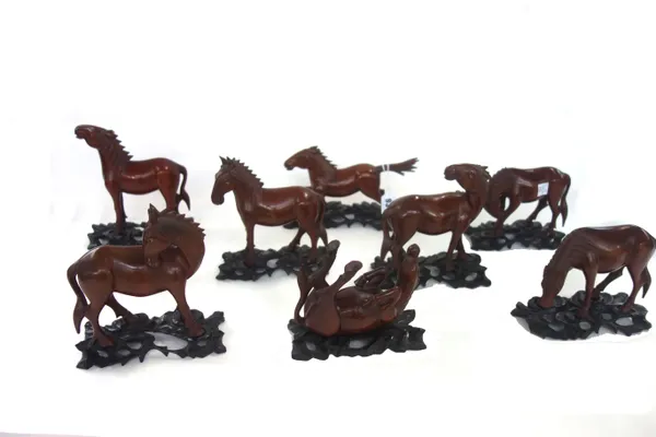 A set of eight Chinese carved wooden horses of Mu Wang, early 20th century, in varying poses, with inset glass eyes, on an ebonised wooden stand, the