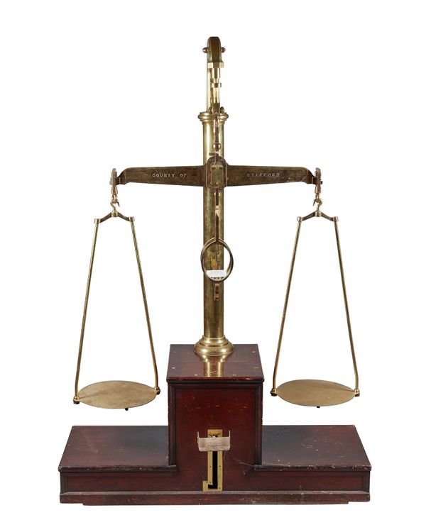 A set of 56lb industrial brass beam scales by De Grave and Co Ltd of London, c. 1900, on a stepped wooden base with foot operated suspension mechanism