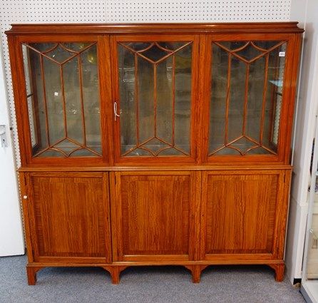 An early 20th century satinwood display cabinet cupboard, with three astragal glazed doors over three panelled cupboards, on block feet, 173cm wide x