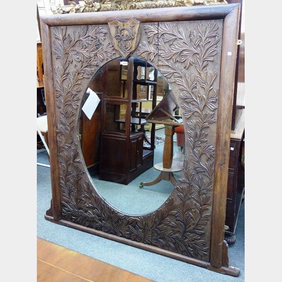 A large 19th century Indian carved hardwood wall mirror, with monogrammed shield crest over oval plate and foliate carved frame, 160cm x 165cm high.