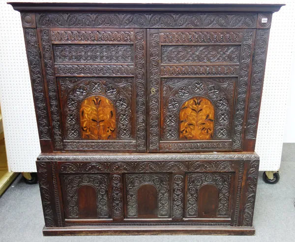 A 17th century and later profusely carved oak hall cupboard, the pair of marquetry inlaid panel doors over a triple panel base, 158cm wide x 159cm hig
