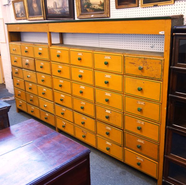 An early 20th century yellow and green painted pine forty two drawer haberdashery cabinet, on block feet, 348cm wide x 185cm high x 28cm deep.