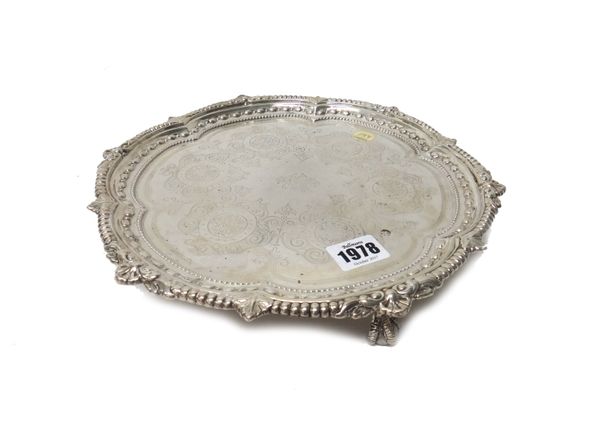 A late Victorian silver salver, of shaped circular form, engraved scroll decoration within a leaf capped gadrooned border, raised on three ball and cl