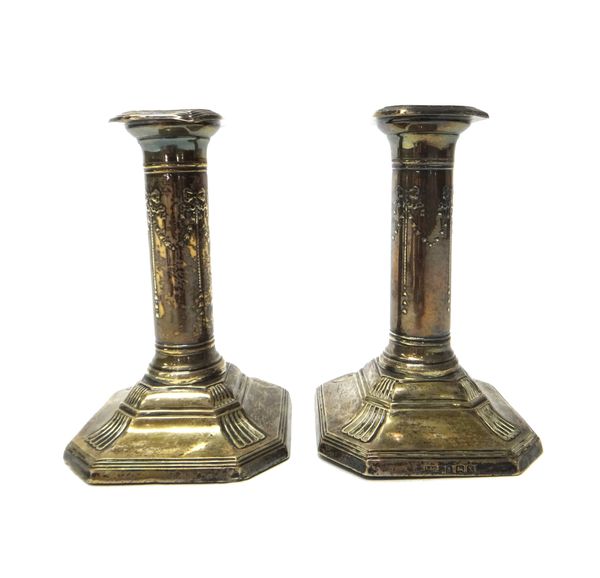 A pair of silver dwarf candlesticks, the cut cornered square loaded bases with reeded borders, the stems decorated with bow swags, Birmingham 1922, he