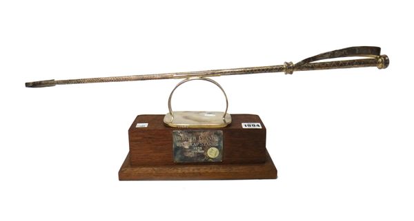 A silver model of a riding crop, on a rectangular stepped wooden plinth with inscribed silver presentation plaque, Sheffield, 1973, gross weight of si