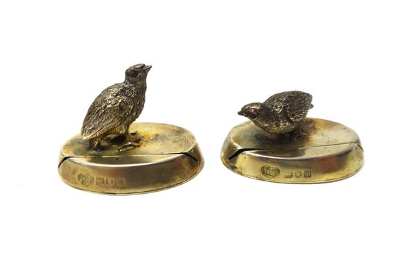 A pair of cast silver gilt menu holders, modelled as game birds, standing on a filled slotted oval base, cased, London,1907.