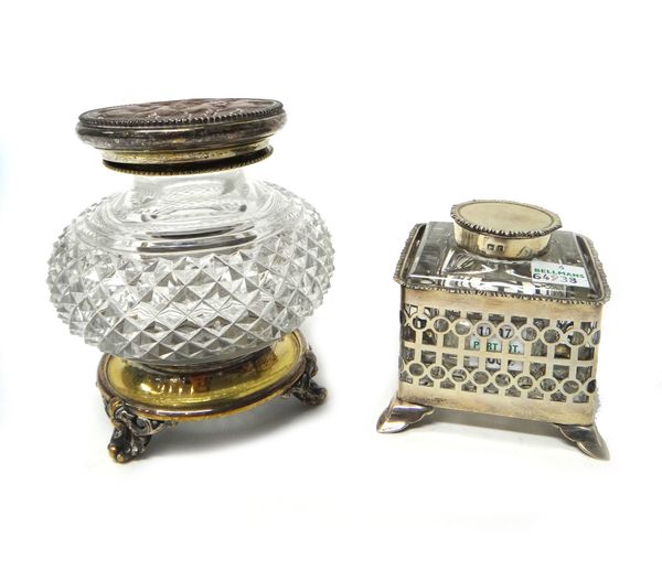 A silver ink bottle stand, of square form, having pierced decoration within a cast rim, raised on four splayed feet, with a silver hinge lidded, squar