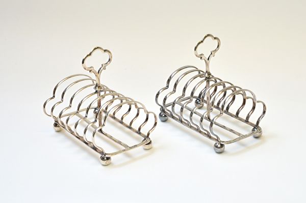 Two similar late Victorian silver toastracks, each of shaped seven bar form, having a loop shaped handle, raised on a rectangular base, with spherical