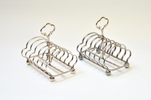 Two similar late Victorian silver toastracks, each of shaped seven bar form, having a loop shaped handle, raised on a rectangular base, with spherical