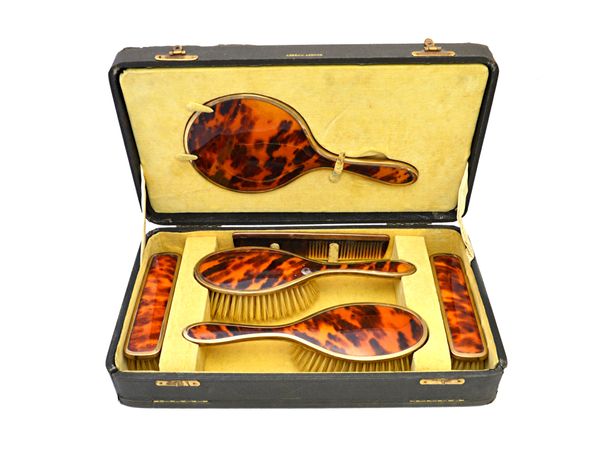 A lady's 9ct gold and tortoiseshell mounted dressing set, comprising; a hand mirror, a pair of clothes brushes, a pair of hairbrushes and a comb, Lond