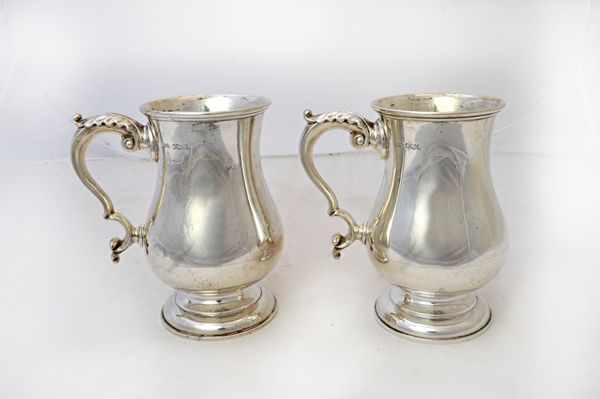 A pair of silver mugs, each of baluster form, with a scrolling handle, raised on a circular foot, by Walker & Hall, Sheffield 1961, height 14.5cm, com