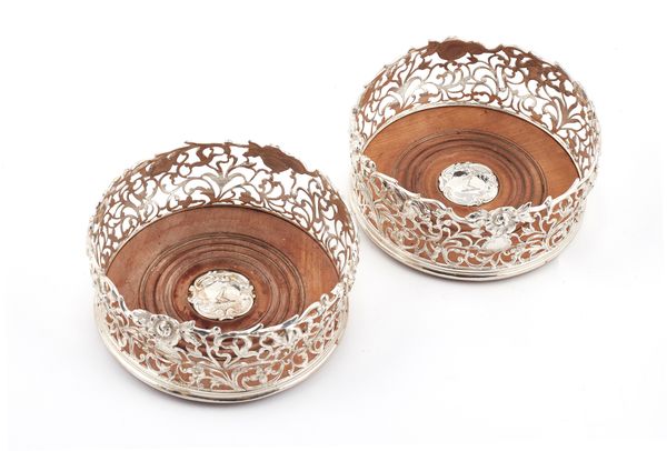 A pair of Victorian silver bottle coasters, of bombe shaped circular form, decorated with floral pierced scrolls within cast floral rims, the turned w