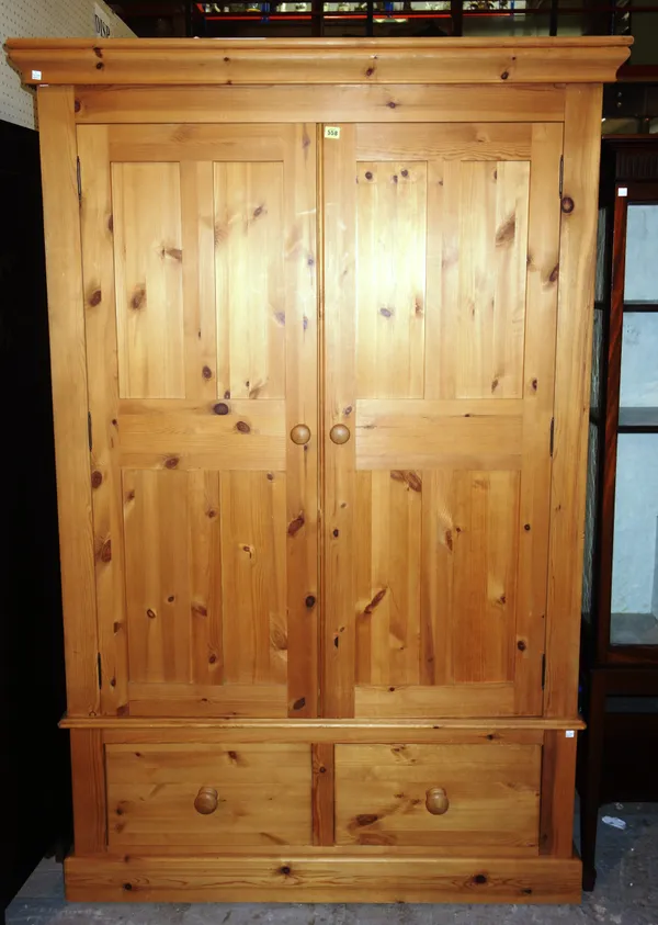 A 20th century pine double wardrobe over a two drawer base, 129cm wide x 204cm high.   M10