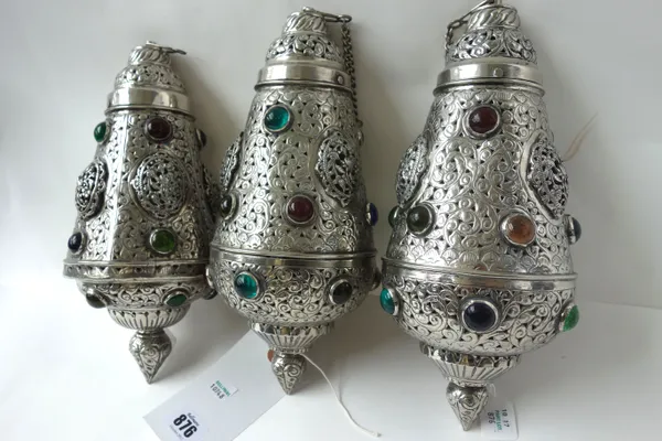 Three Islamic silver hanging lamps, decorated with pierced raised roundels and inlaid with coloured glass and agate cabochons, 34cm long. (3)