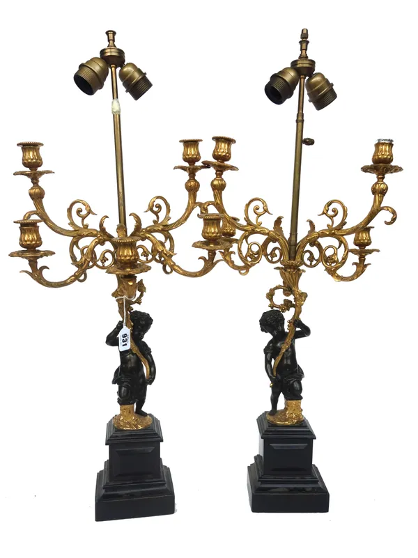 A pair of French ormolu and patinated bronze five light figural candelabra (converted to table lamps), each with central putto figure holding a floral