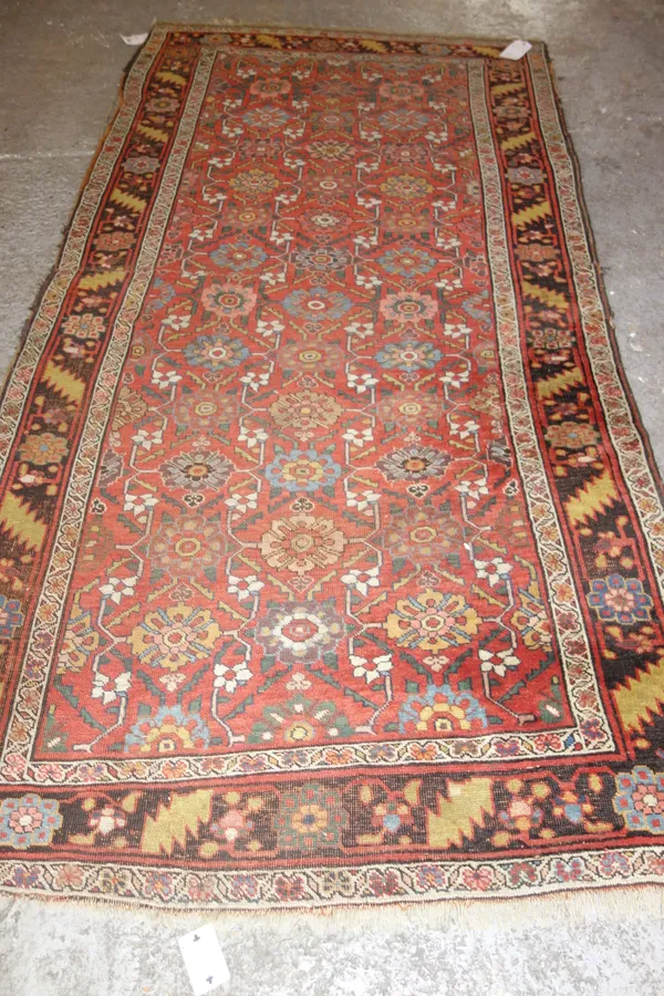A North West Persian runner, the madder field with an allover flower design, a black flower and leaf border, 262cm x 130cm, (a.f).