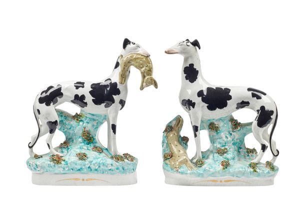 A pair of Staffordshire pottery models of `Disraeli' greyhounds, 19th century, each painted with black patches, modelled standing , one with a hare in