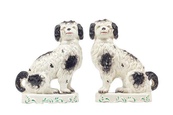 A pair of Staffordshire pipe smoking spaniels, 19th century, each black and white dog modelled with a pipe in its mouth, front legs separately moulded