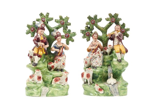 A pair of Staffordshire 'Songsters' pearlware figure groups, depicting a musical shepherd and shepherdess, early 19th century, each seated beneath a b