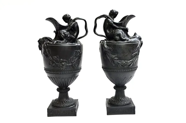 A pair of Wedgwood basalt `wine' and `water' ewers, late 19th century, with figural handles and applied masks, over a fluted socle and square base, im