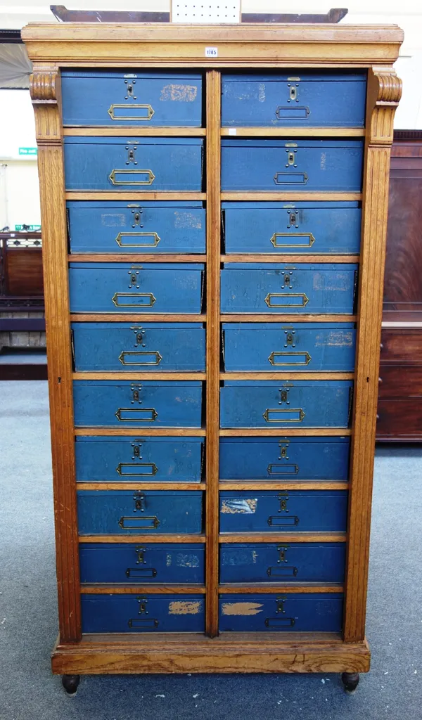 An early 20th century French oak cartoniere, the twin locking bars enclosing two rows of ten cartons, on turned feet, 101cm wide x 39cm deep x 204cm h
