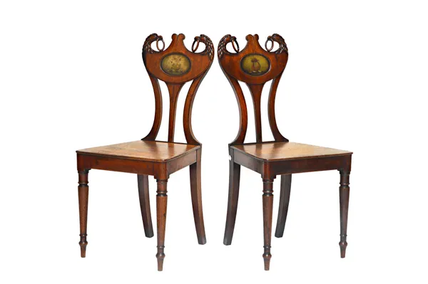 A pair of late George III mahogany hall chairs, with opposing eagle carved back about the painted panel, over solid seat on four turned supports, 42cm