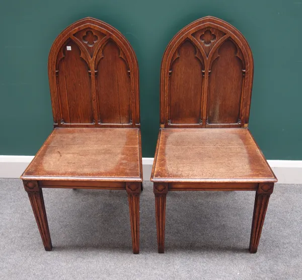A pair of Victorian Gothic Revival carved oak arch back hall chairs, on tapering supports, each 49cm wide x 93cm high, (2).