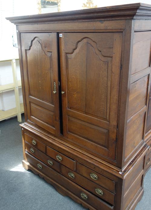 A mid-18th century oak press cupboard, the pair of arch panel doors over six various drawers, on shaped plinth base, 144cm wide x 190cm high.