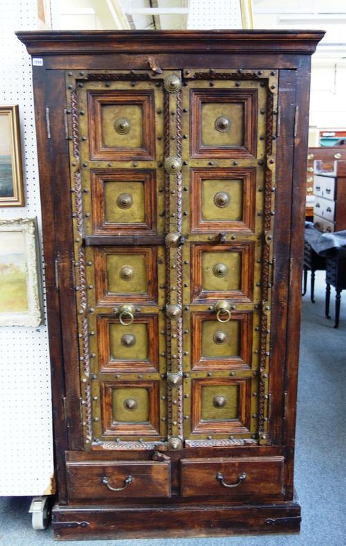 A 19th century and later Indian hardwood and brass mounted cupboard, the pair of doors each with five recessed panels over a pair of short drawers on