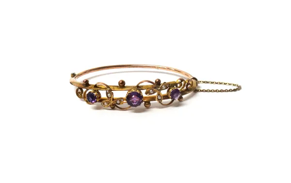 A 9ct gold, amethyst and seed pearl set oval hinged bangle, the front with scroll and trefoil pierced motifs, between beaded sides, on a snap clasp, C