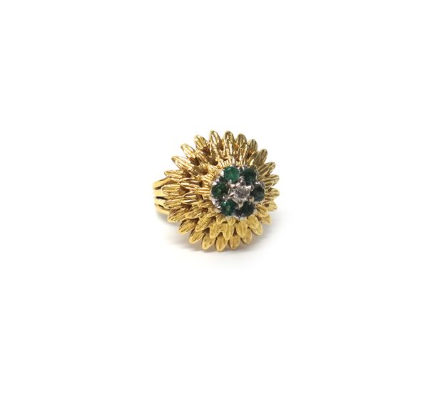 A gold, emerald and diamond cluster ring designed as a flowerhead, claw set with the circular cut diamond in a surround of six circular cut emeralds,