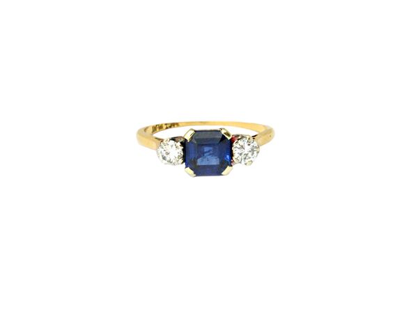 A gold and platinum, sapphire and diamond set three stone ring, claw set with the cut cornered square step cut sapphire at the centre, between circula