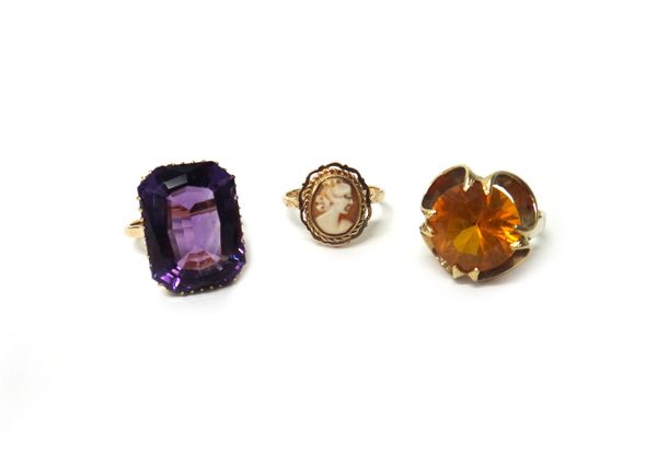 A gold ring, claw set with a cut-cornered rectangular cut amethyst, detailed '18ct', a 9ct gold ring, claw set with a circular cut orange gem and a go