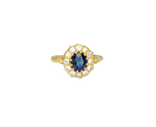 A gold, sapphire and diamond cluster ring, claw set with the oval cut sapphire at the centre, within a diamond set twelve stone surround, between diam