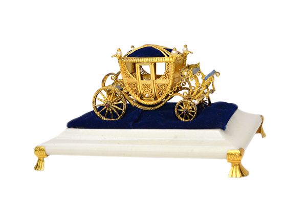 A limited edition silver gilt, cultured pearl, lapis lazuli and cabochon garnet set model of a four wheeled coach, having a pin cushion top, displayed