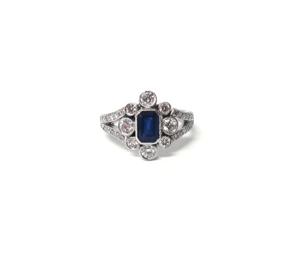 A white gold, sapphire and diamond cluster ring, mounted with the cut cornered rectangular step cut sapphire at the centre, in a surround of eight cir