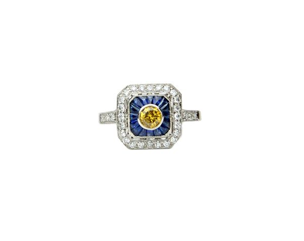 A platinum, diamond, yellow diamond and sapphire set ring, in a cut cornered square panel shaped design, collet set with the circular cut yellow diamo