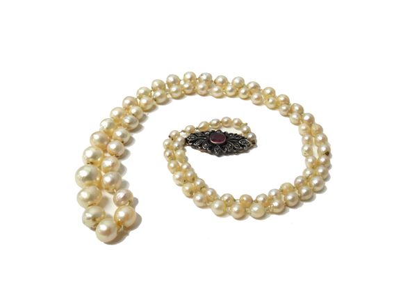 A single row necklace of graduated cultured pearls, on a diamond and garnet set clasp, in a pierced oval design.