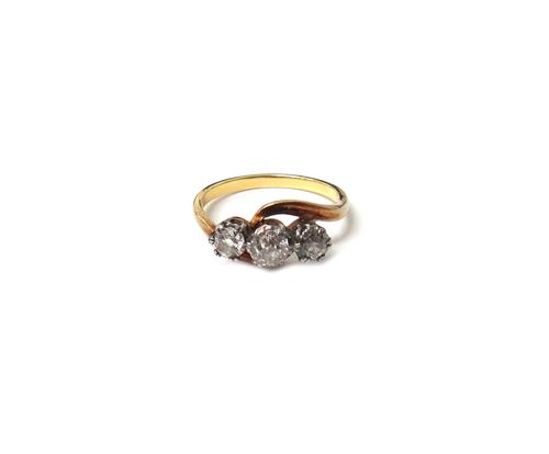 A gold and diamond three stone ring, claw set with a row of cushion shaped diamonds and with the principal diamond mounted at the centre, in a crossov