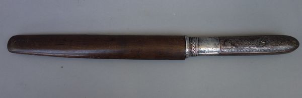 A Burmese shan knife, 20th century, with silver edged steel blade (30cm), silver hilt and silver inlaid wooden handle in a wooden sheath.  Illustrated