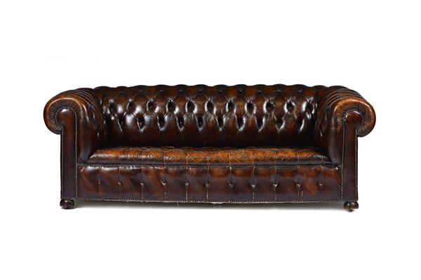 A brown leather button upholstered Chesterfield sofa, with roll over arms, on bun feet, 210cm wide x 68cm high x 90cm deep.  Illustrated