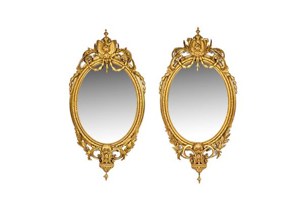 A pair of 19th century gilt framed oval wall mirrors, each with floral swag shield crest and marbled frame, 58cm wide x 115cm high, (2).  Illustrated