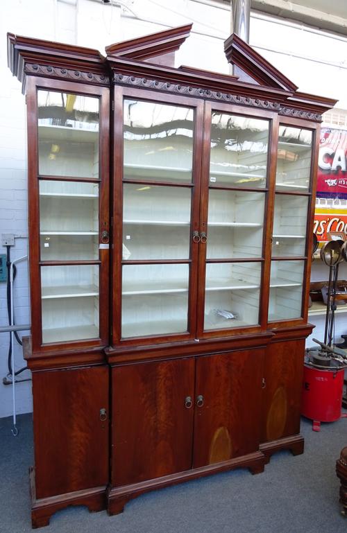 A George II and later mahogany breakfront bookcase cabinet, the broken architectural cornice over four glazed doors and four cupboards, on bracket fee