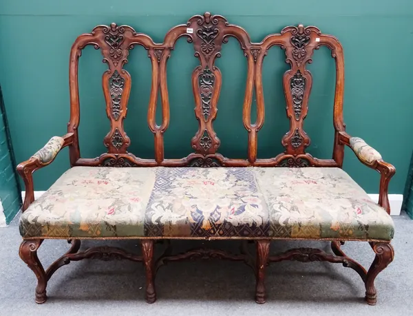A walnut framed Queen Anne style triple chair back open arm sofa, on carved hoof feet, united by shaped stretcher, 164cm wide x 125cm high.