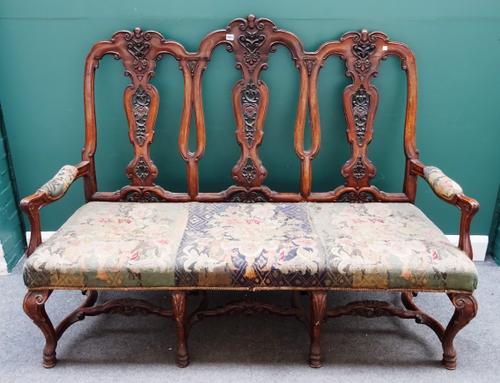 A walnut framed Queen Anne style triple chair back open arm sofa, on carved hoof feet, united by shaped stretcher, 164cm wide x 125cm high.