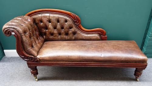 A Victorian mahogany framed scroll back chaise longue, with button brown leather upholstery, on turned supports, 180cm wide x 90cm high.